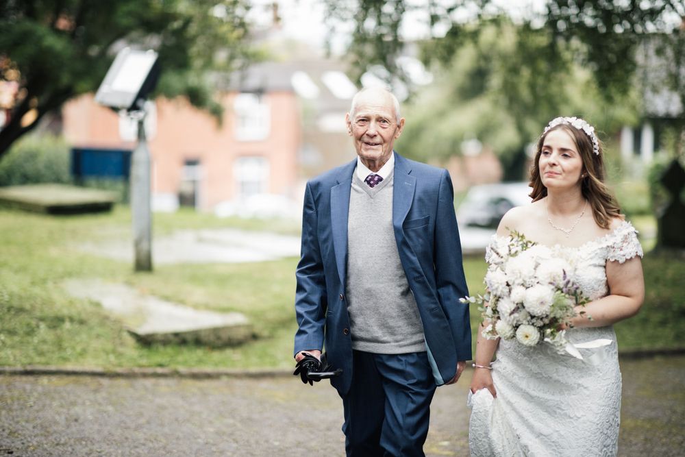 Two people walk together on a garden path on a sunny wedding day.
