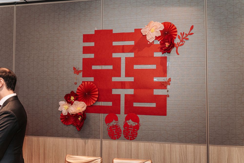 A red double happiness Chinese character wall decoration with floral accents mounted on a gray wall.