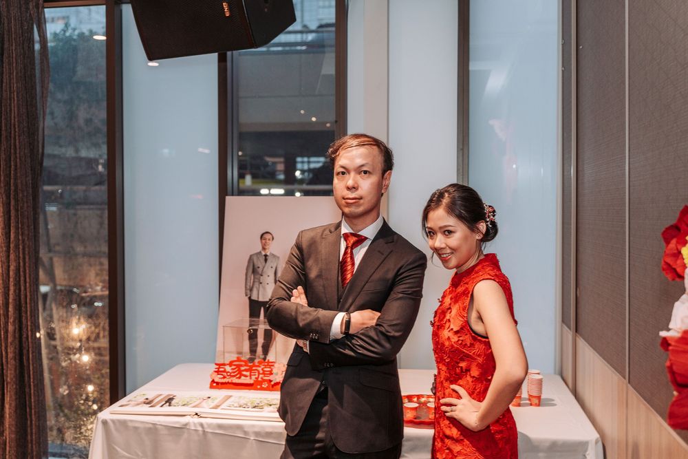 Two people in formal attire stand next to a cake at a special event with a display window behind them.