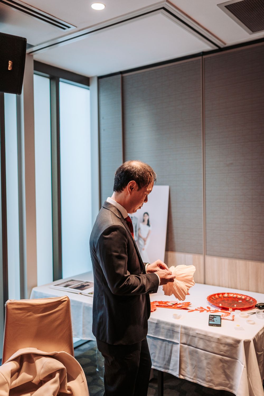 A person in a dark suit examines items on a white tablecloth in a modern office room with gray walls.