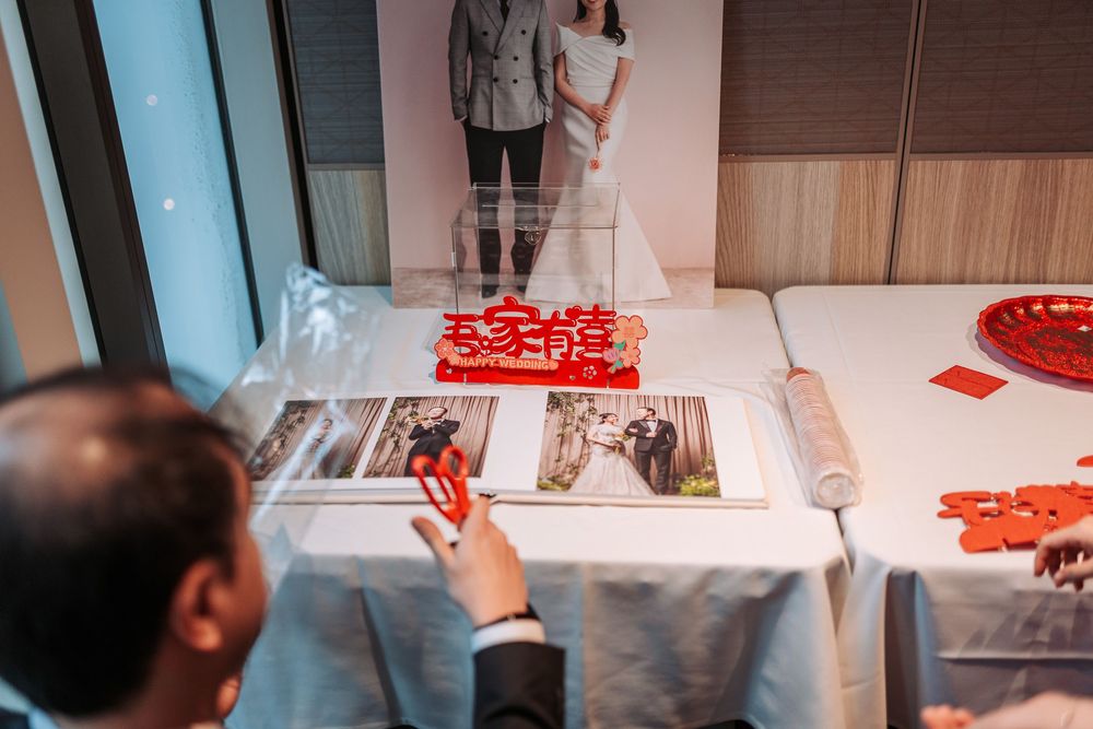 Wedding guests look at photo displays and decor items arranged on a white tablecloth at a reception.