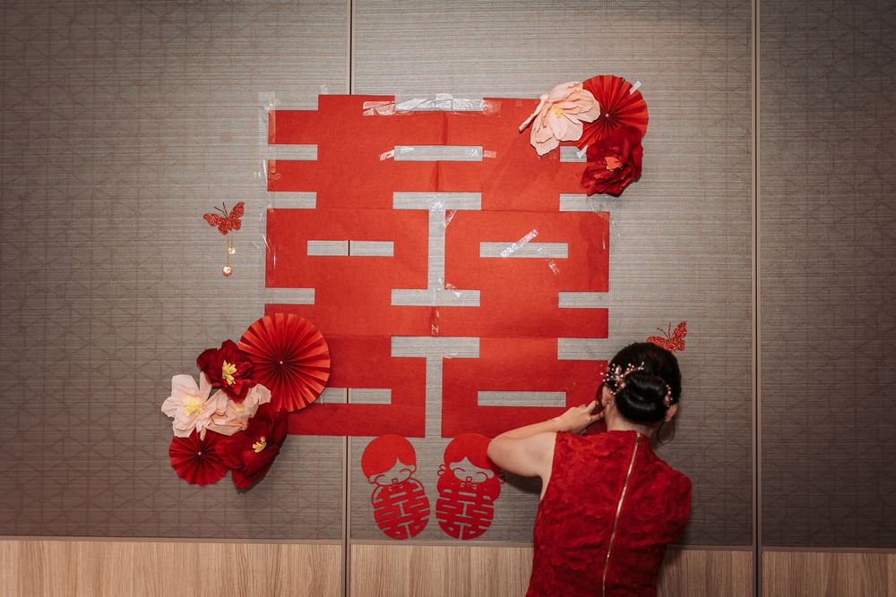 Red and white traditional Chinese double happiness symbol and floral decorations on a wall for a wedding celebration.
