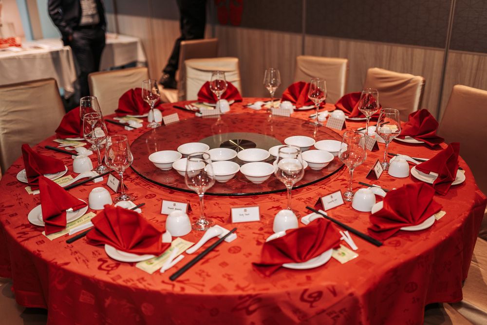 Elegant round dining table set with red tablecloth, white dinnerware, and festive red napkins in a banquet setting.