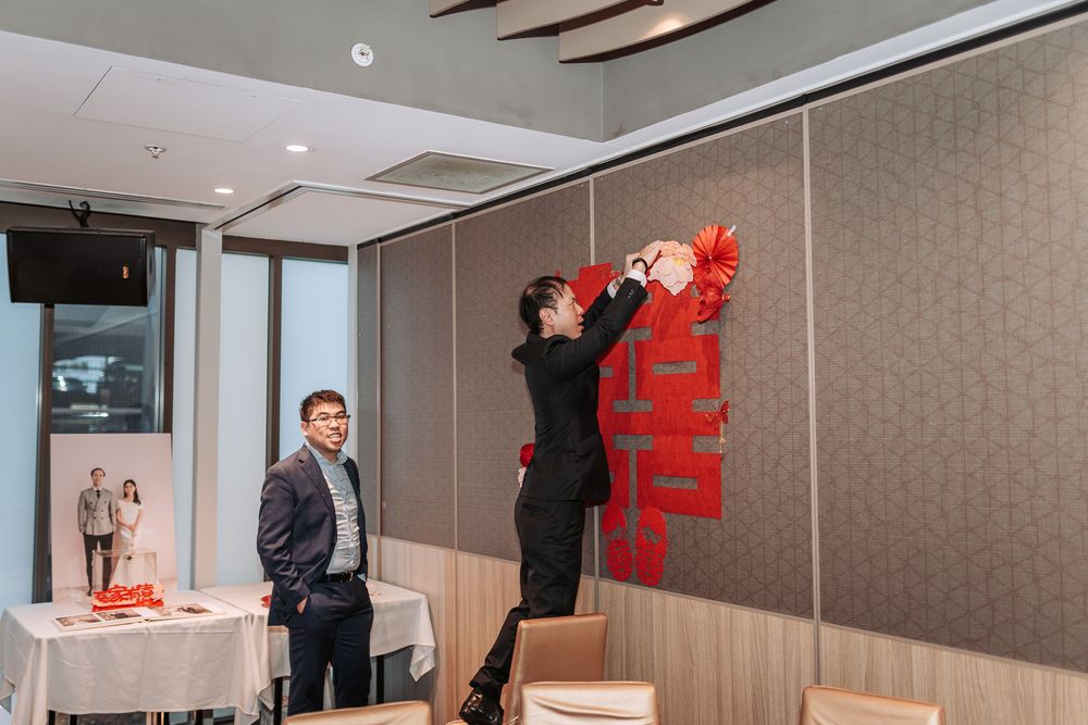Decorations being placed on a gray wall in a modern meeting room with wood paneling and ceiling lights.