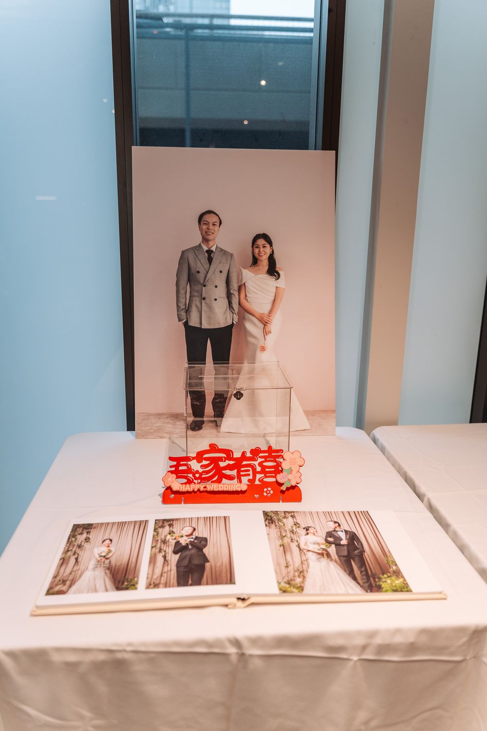 Wedding photo setup with portrait display and photo album on white tablecloth with red Chinese wedding decorations.