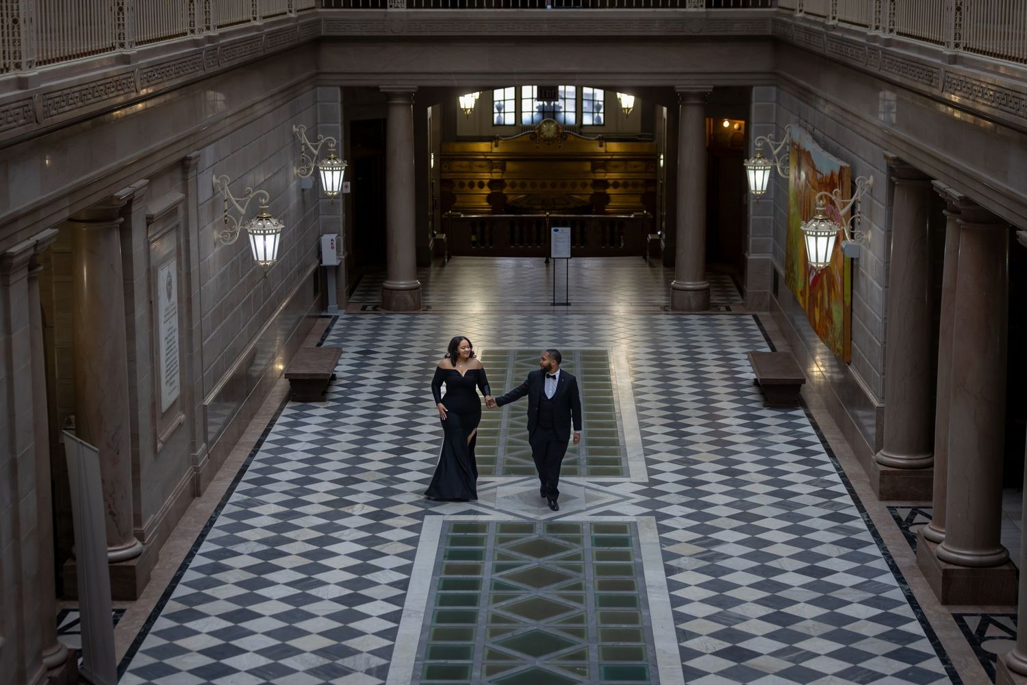 Two people stand alone in a grand hallway with checkered marble floors and classical architecture lit by wall sconces.