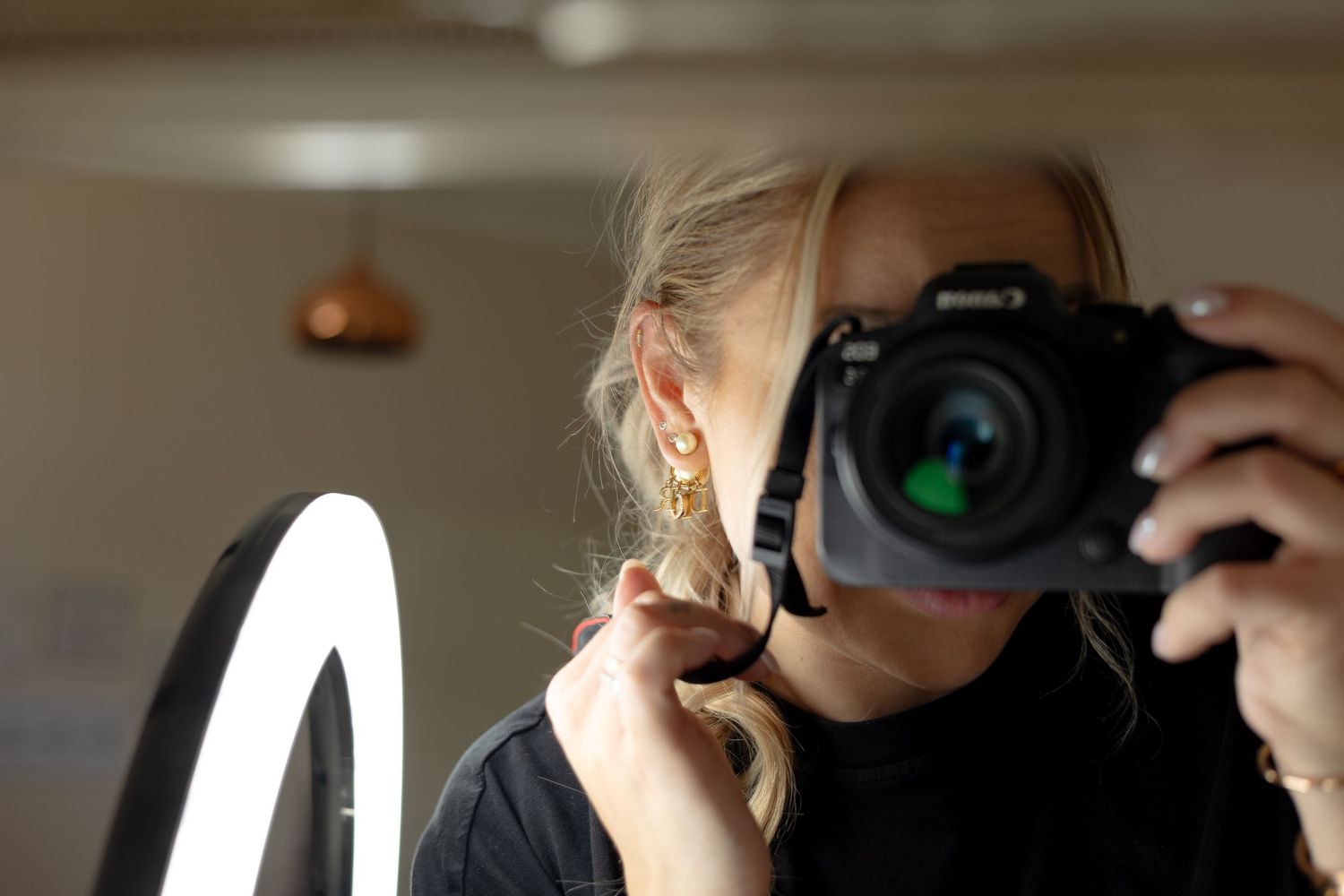 Selfie portrét fotografky s fotoaparátem v ruce, pohled do objektivu s odrazem v zrcadle.