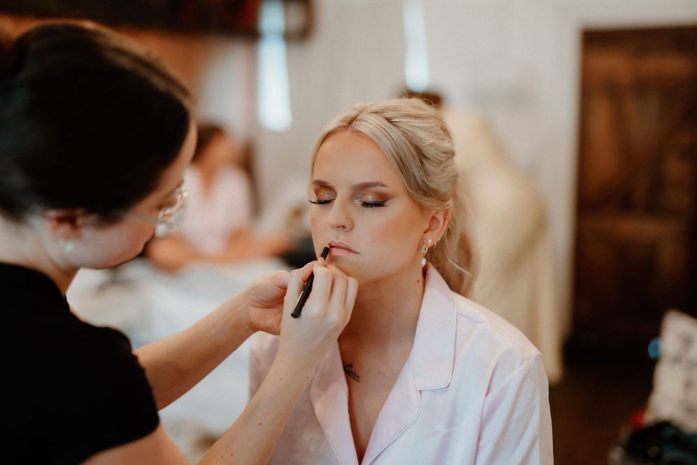 A makeup artist applies cosmetics to a person wearing a white robe during wedding preparations.
