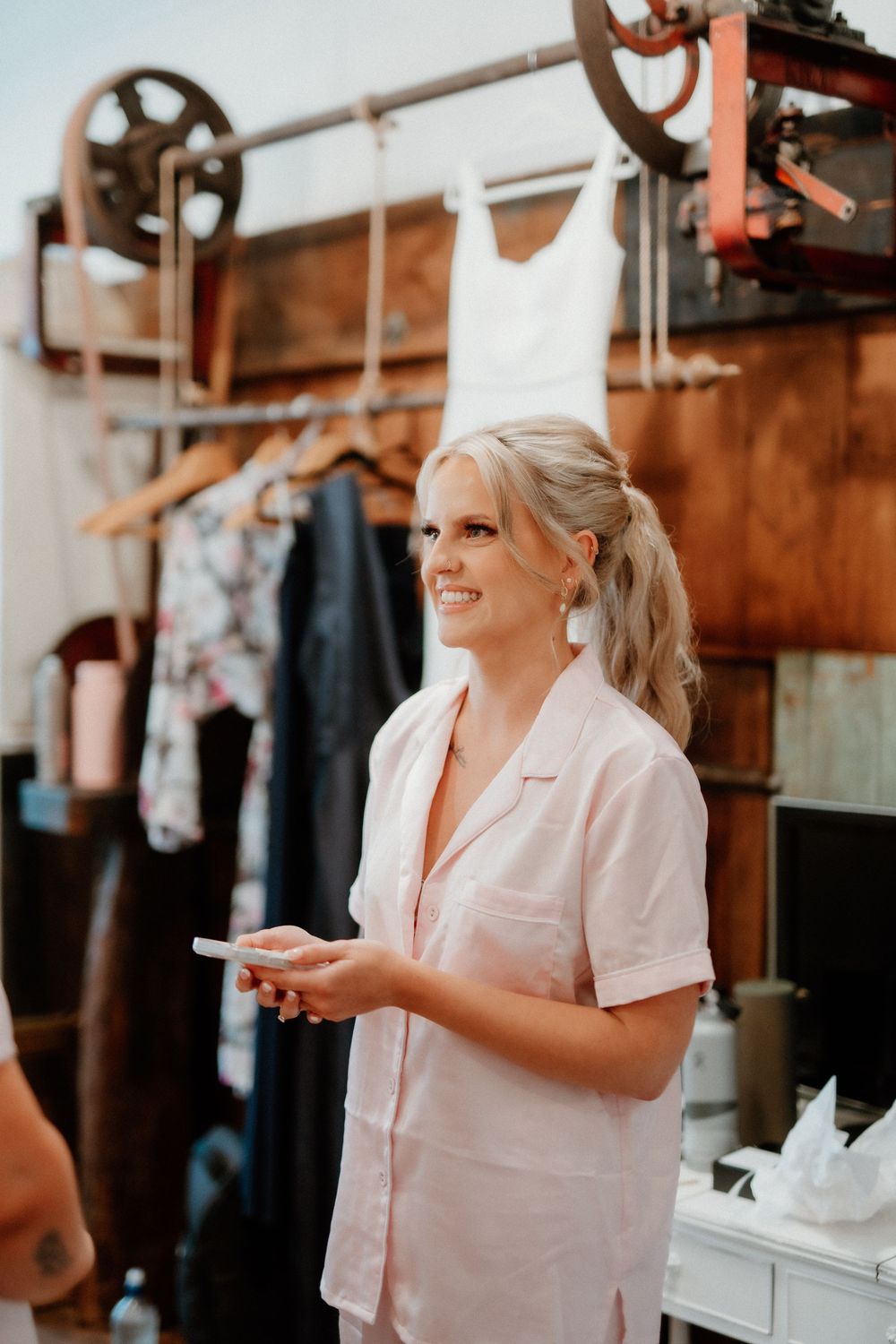 Bride in white robe smiling while holding phone during wedding preparations.