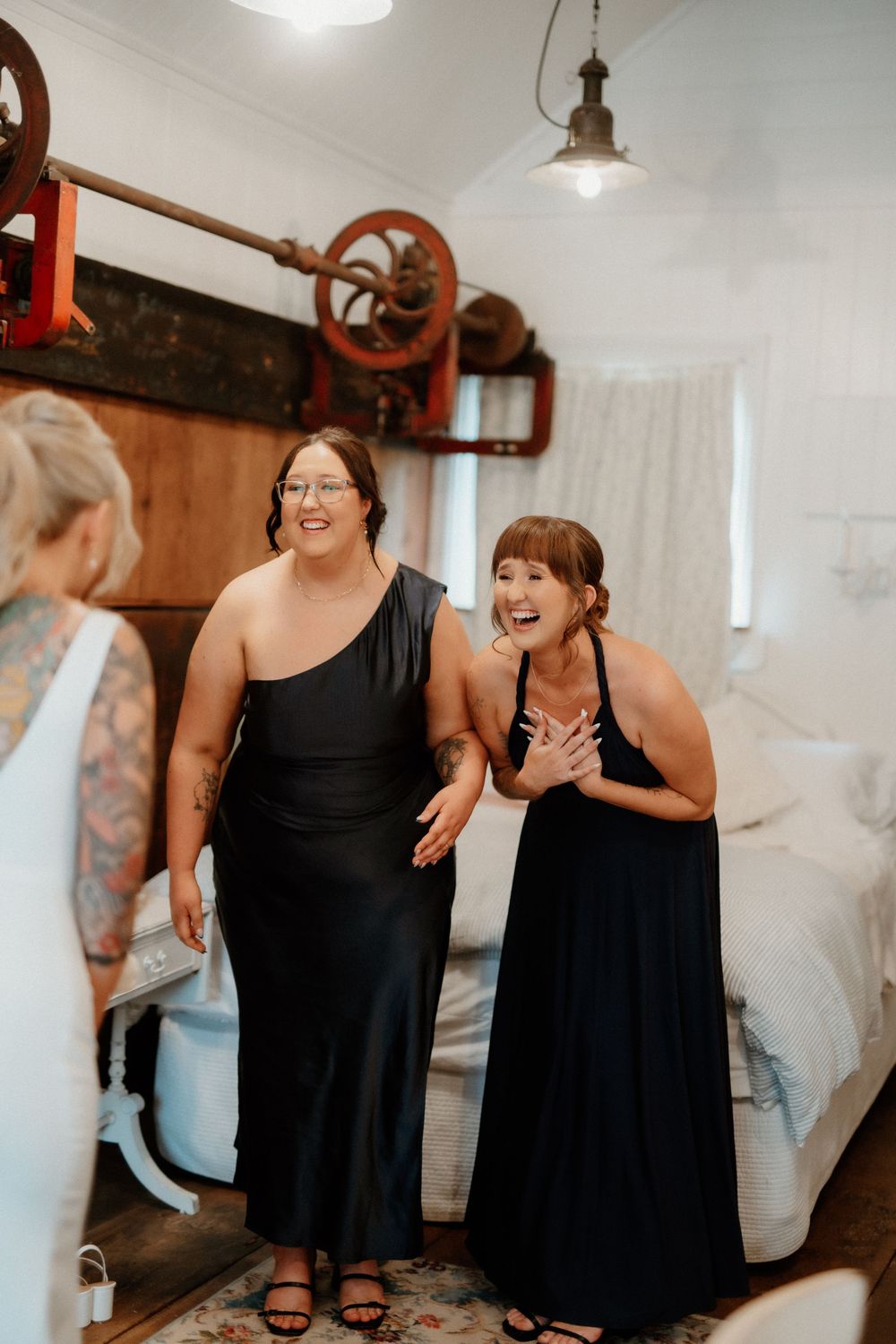 Two bridesmaids in black gowns sharing a joyful laugh during wedding preparations.