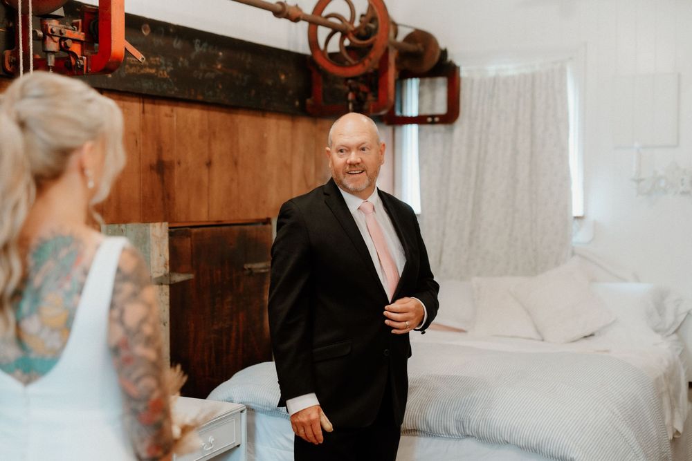 A touching first look moment between father and daughter before a wedding in a rustic bedroom setting.