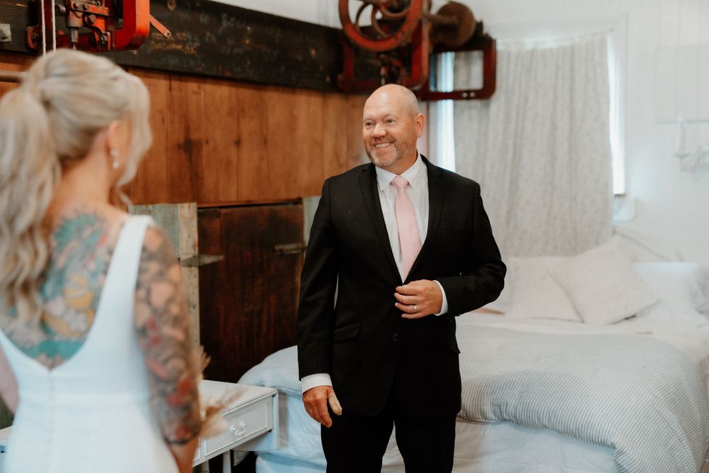 A person in a black suit reacts emotionally during a first look moment in a bedroom setting.