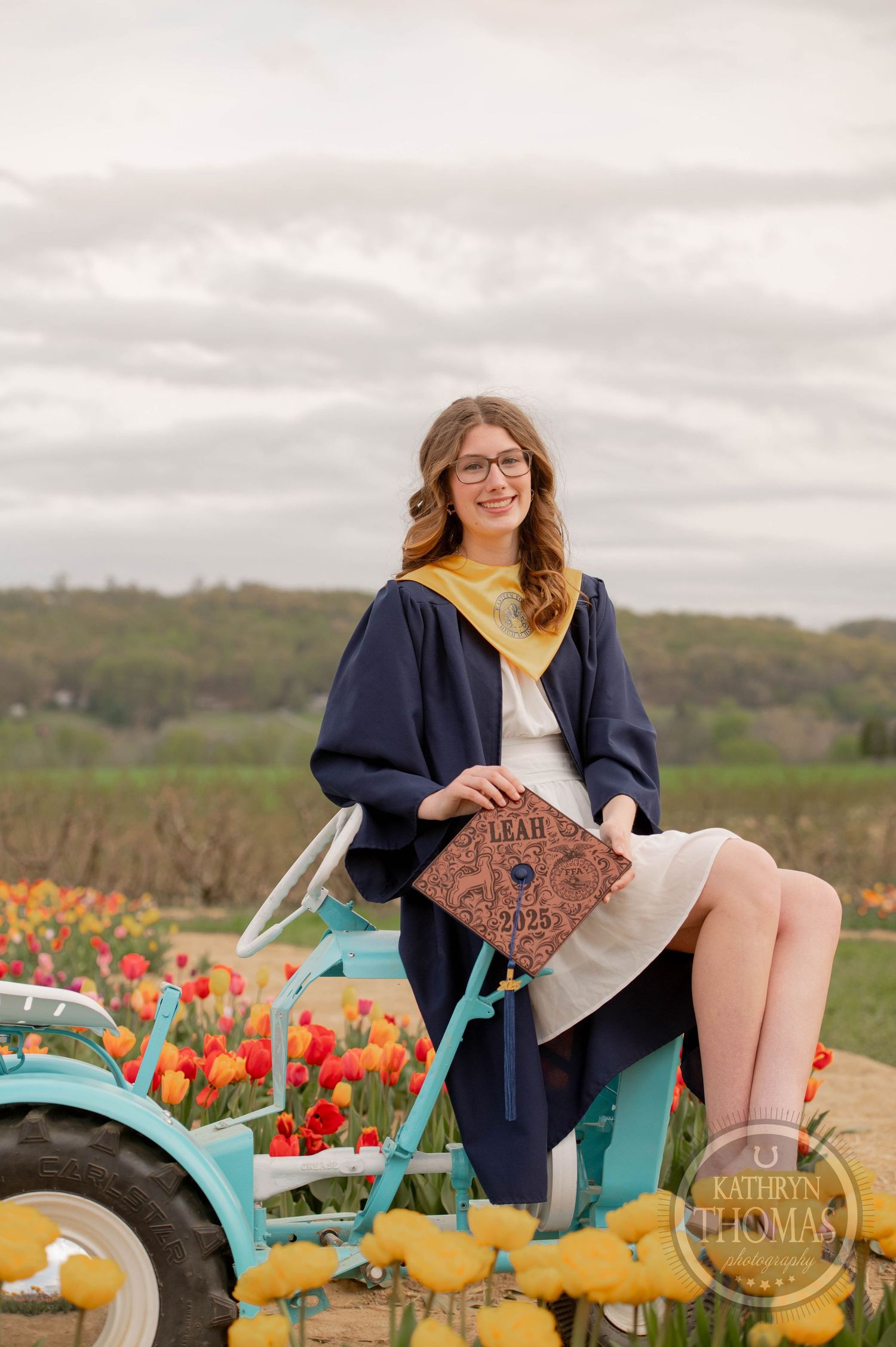 A person sits on a turquoise vintage tractor amid vibrant tulip fields on an overcast autumn day.