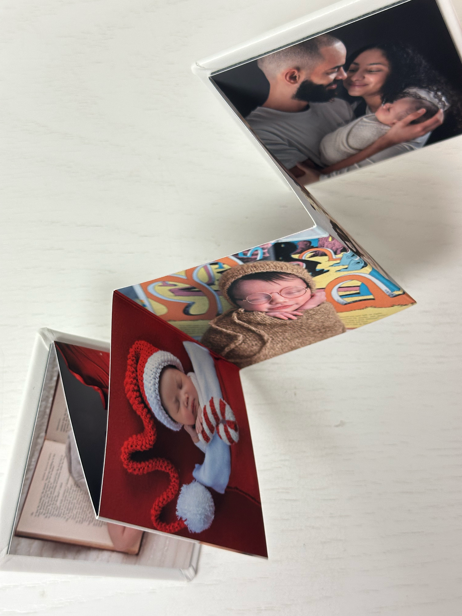 Three small folded photo books displaying family portraits including a newborn baby, couple, and holiday-themed infant photo.