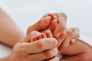 Close-up of adult hands tenderly holding baby feet against white background.