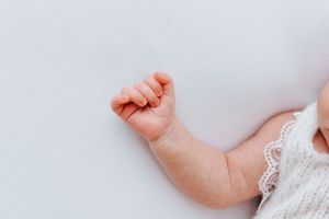 Delicate lace details and baby hands against white background.