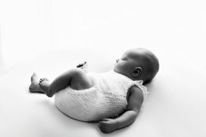 Infant lying on side wearing white onesie against light backdrop.