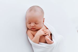 Peaceful sleeping newborn baby in white swaddle against neutral background.
