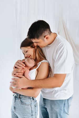 Close up of a tender embrace between two people wearing jeans and white shirts against a light background.