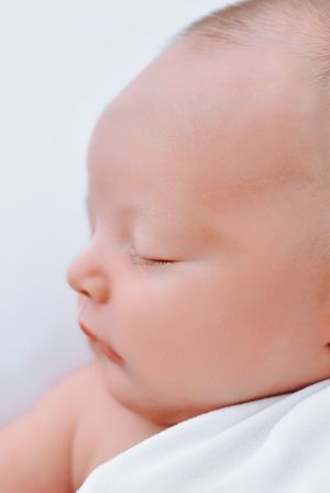 Close up profile view of sleeping baby's face against soft white bedding.