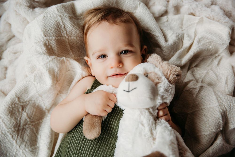 A sweet moment captured of a baby hugging a white stuffed animal on textured bedding.