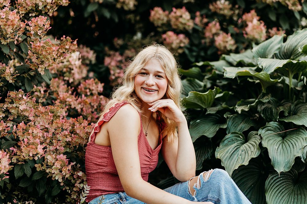 A relaxed outdoor portrait among flowering plants and foliage on a sunny day.