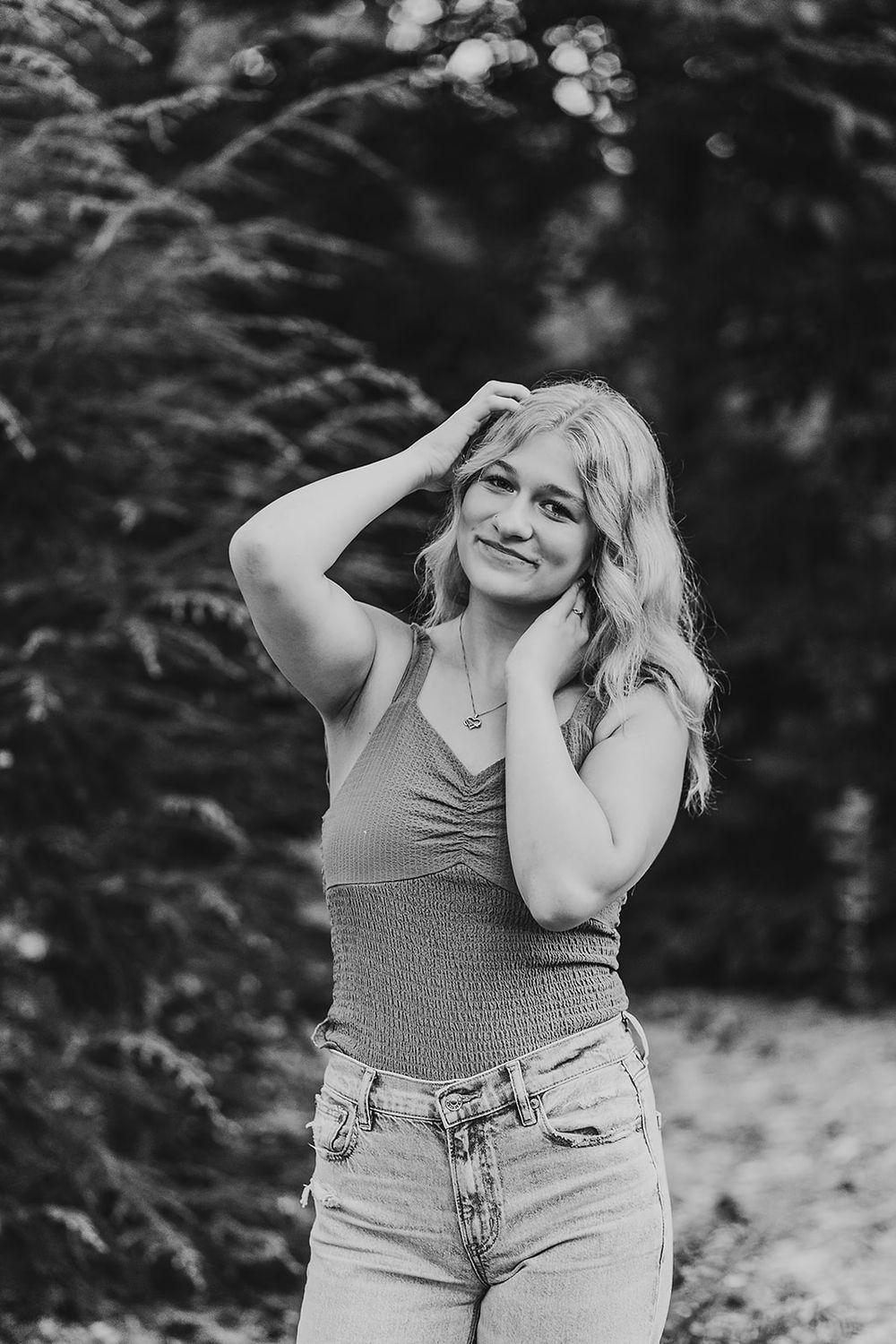 Black and white portrait of someone in a casual outfit posing against a natural outdoor background.