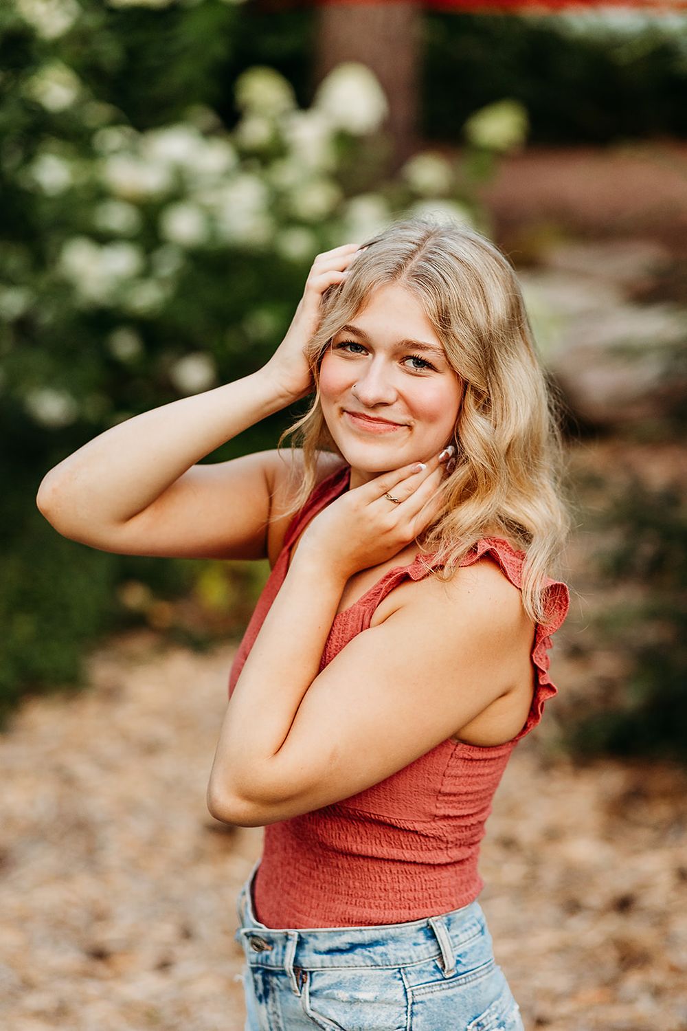 Casual outdoor portrait in a garden setting with someone wearing a coral top and jeans.