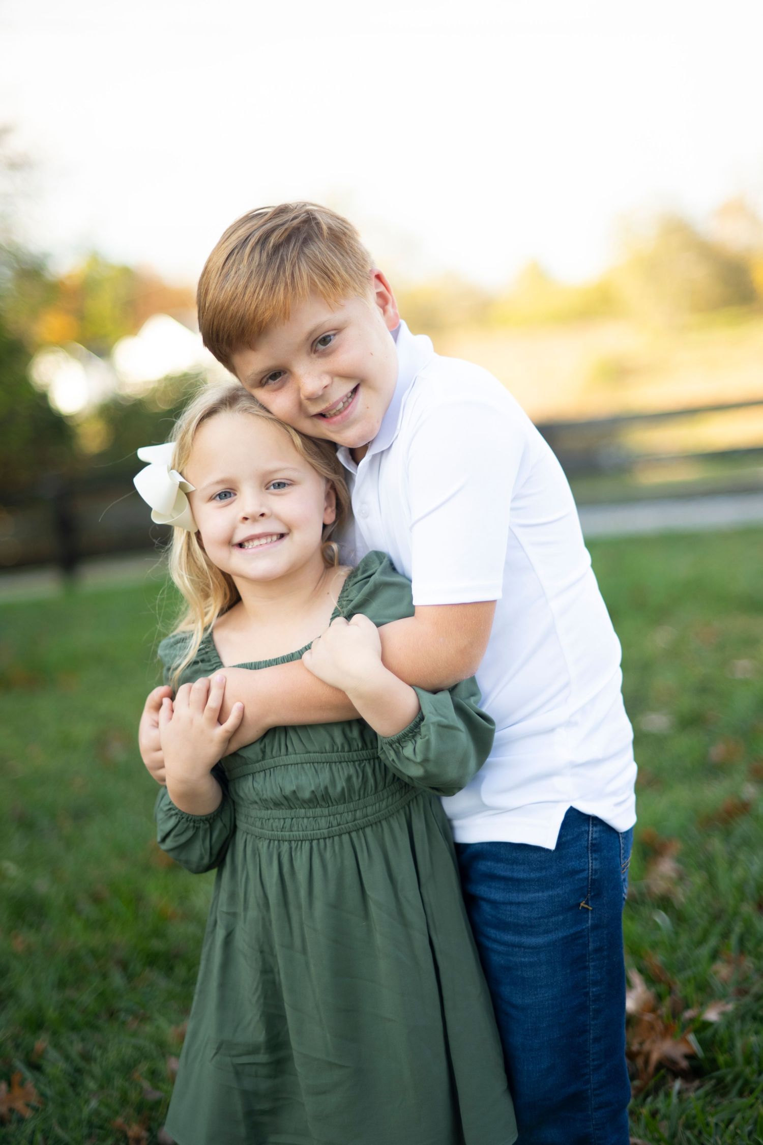 Two children sharing a sweet embrace outdoors in a sunlit garden setting at Muletown Farm in Columbia, TN.