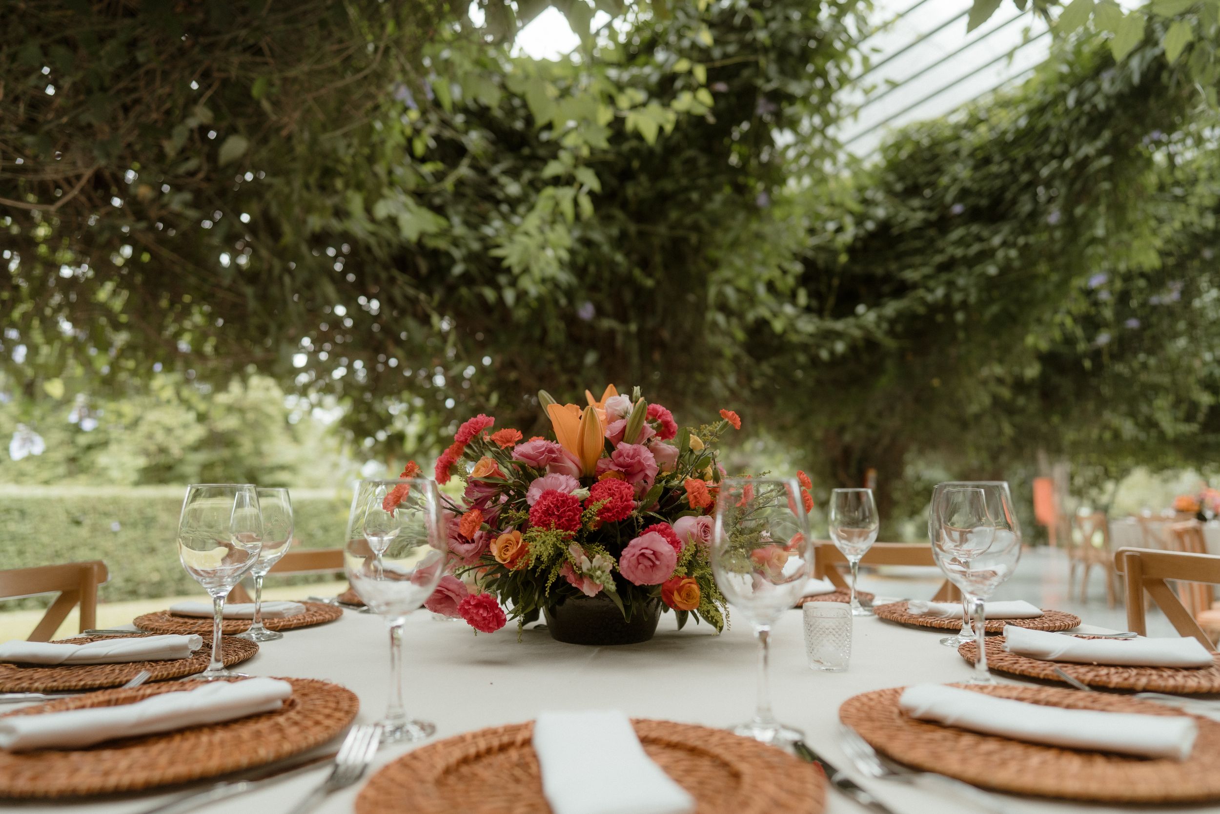 Elegant outdoor wedding table setting with vibrant red floral centerpieces and natural greenery.
