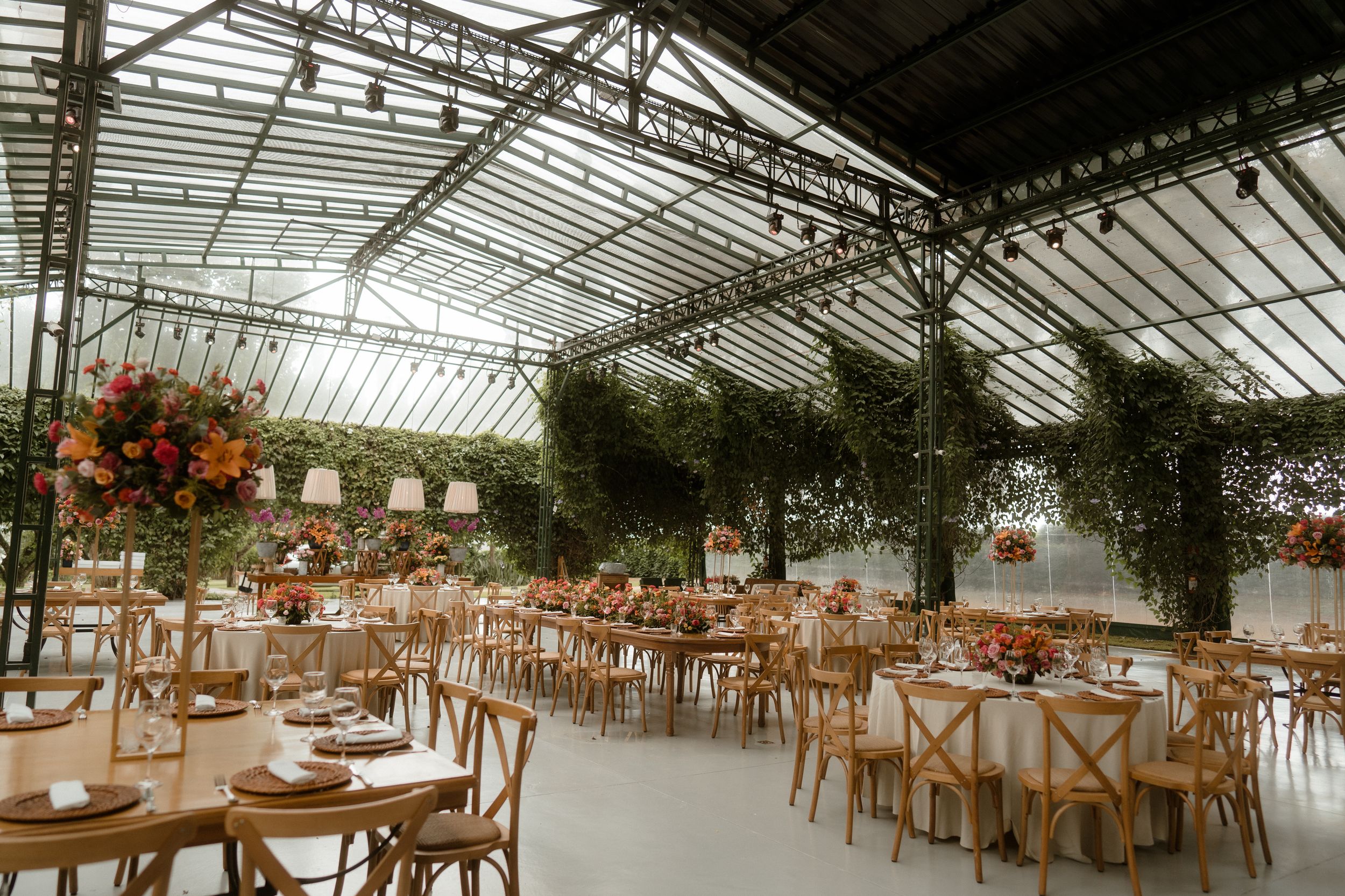 Large greenhouse venue with wooden tables and chairs set up for a wedding reception.