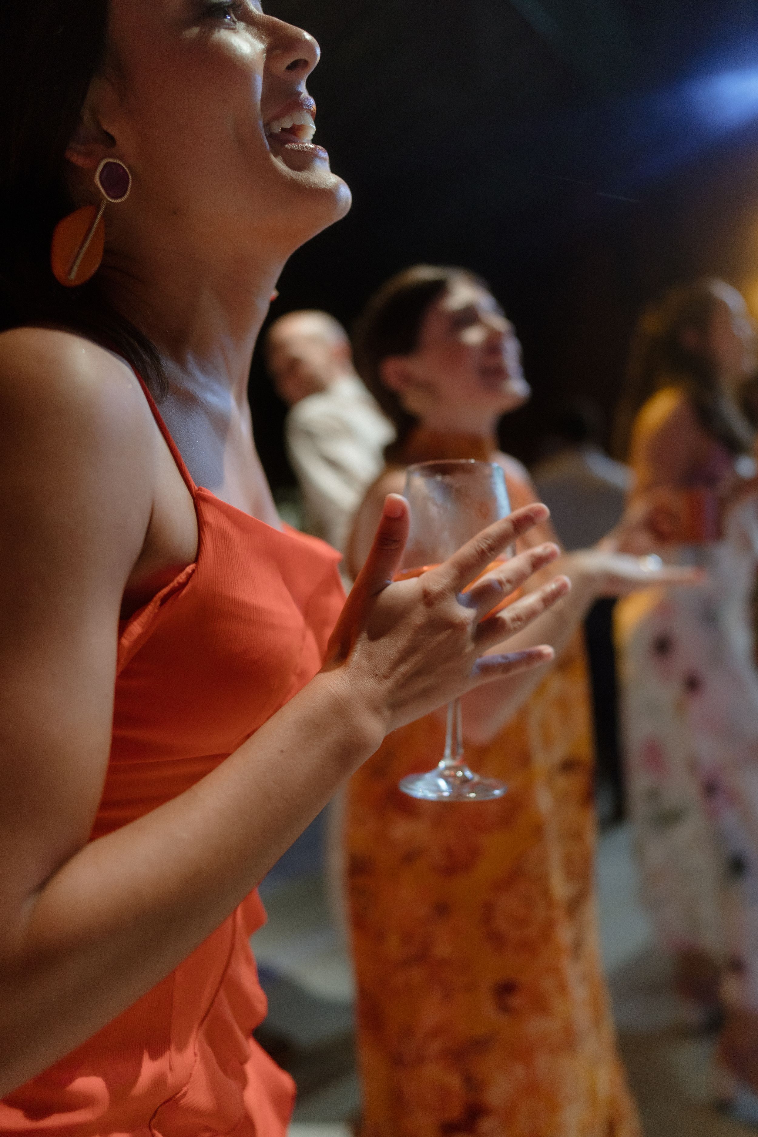 Woman in coral dress enjoying a celebration with wine glass in hand under ambient lighting.