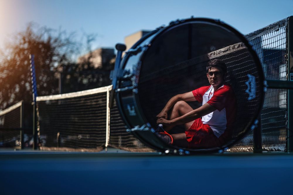 Basketball player in red jersey seen through circular tunnel at outdoor court during sunset practice session.