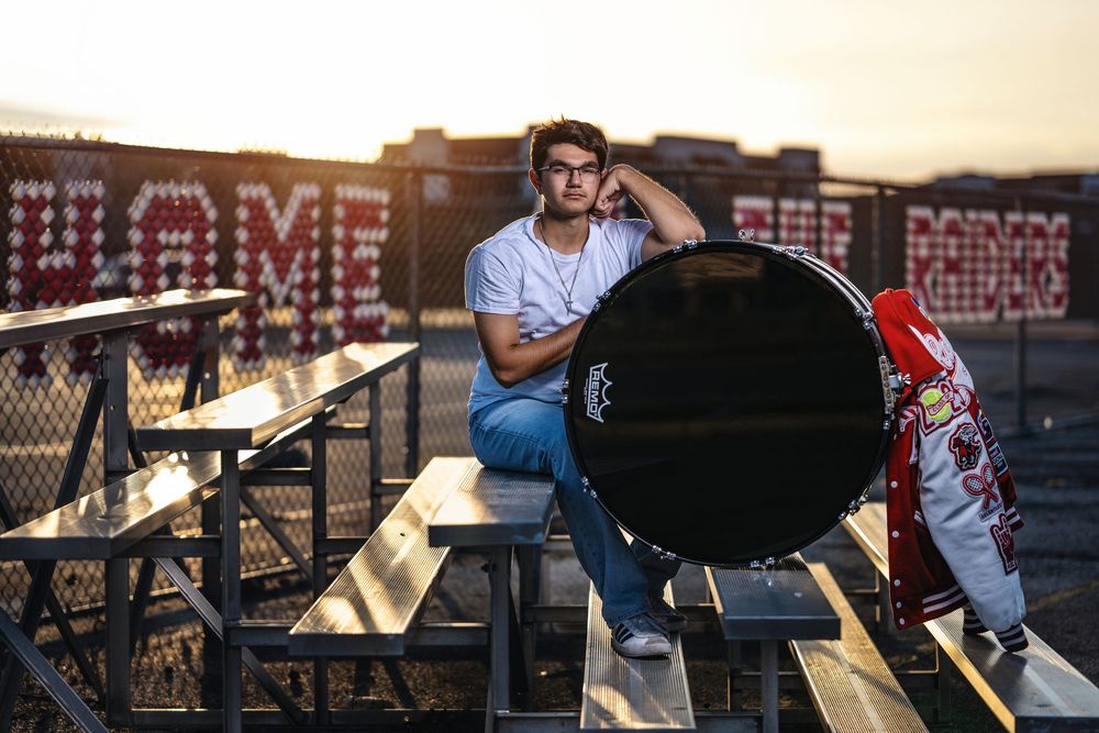 Person in blue jeans sits on bleacher seats next to a large grill during golden hour on a rooftop.