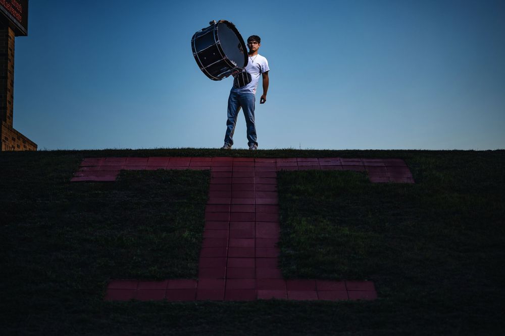 A figure stands on top of a building against a deep blue sky while holding a large circular object at dusk.
