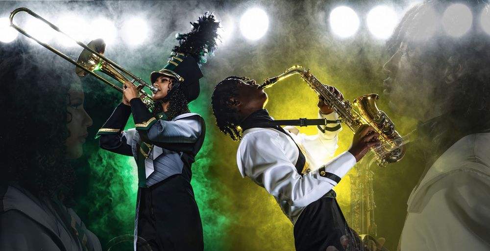 Two musicians perform on stage with saxophones amidst dramatic green and yellow lighting effects during a live show.