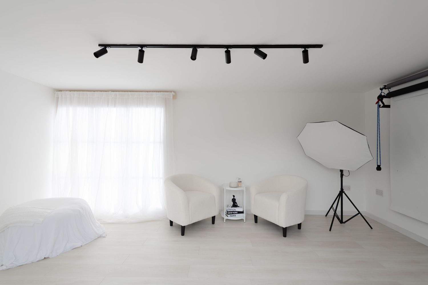 Professional photography studio interior with white chairs, lighting equipment and sheer curtains in a bright minimal space.