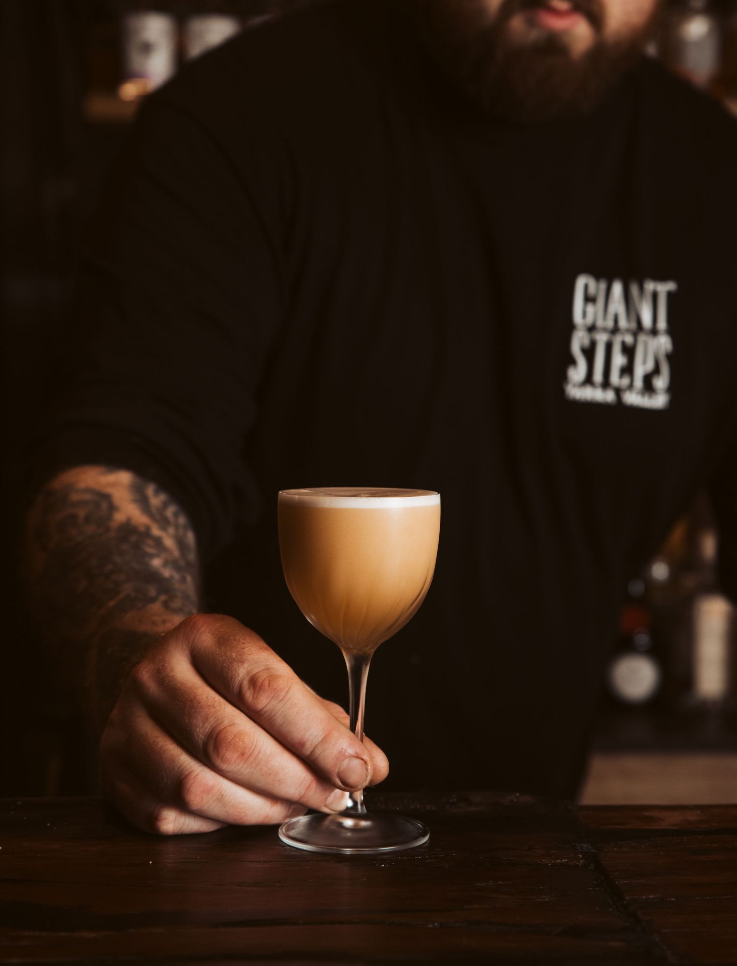 Craft cocktail with foam top held at intimate bar with moody lighting