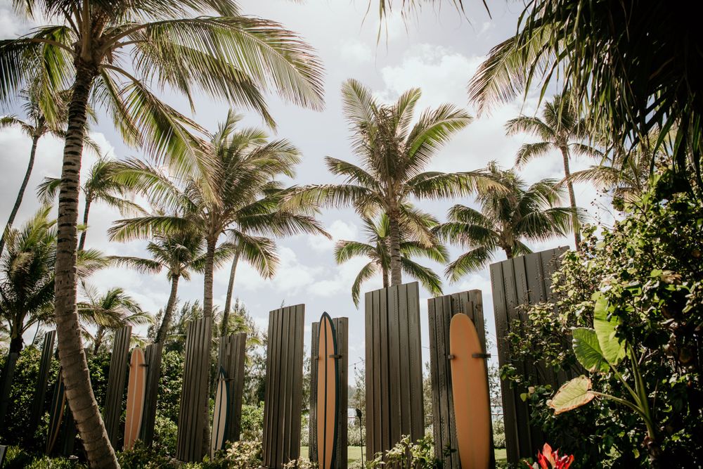 Tall metallic pillars stand among tropical palm trees at a resort with modern architecture in the background.