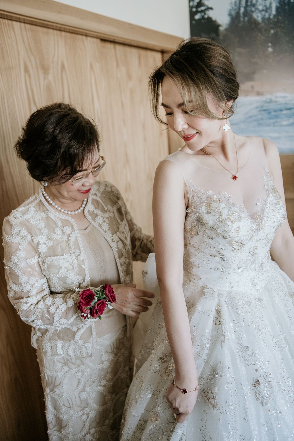 A tender moment between a person in a white lace wedding dress and another in a white embroidered gown holding a pink bouquet.