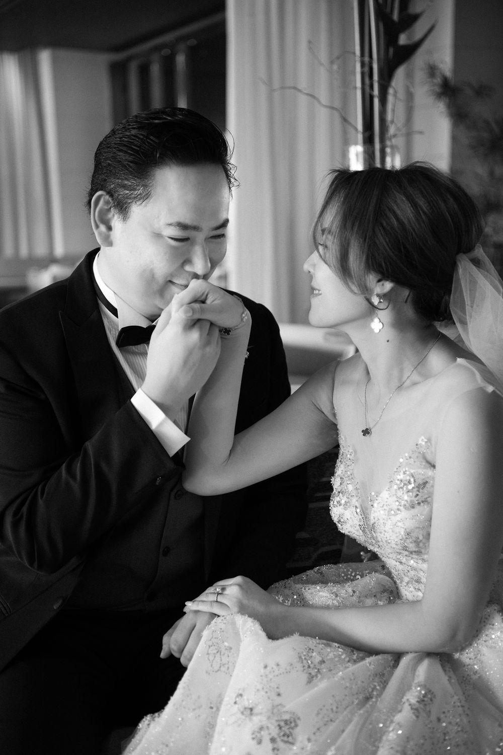A romantic black and white wedding photo showing an affectionate moment between newlyweds in formal attire.