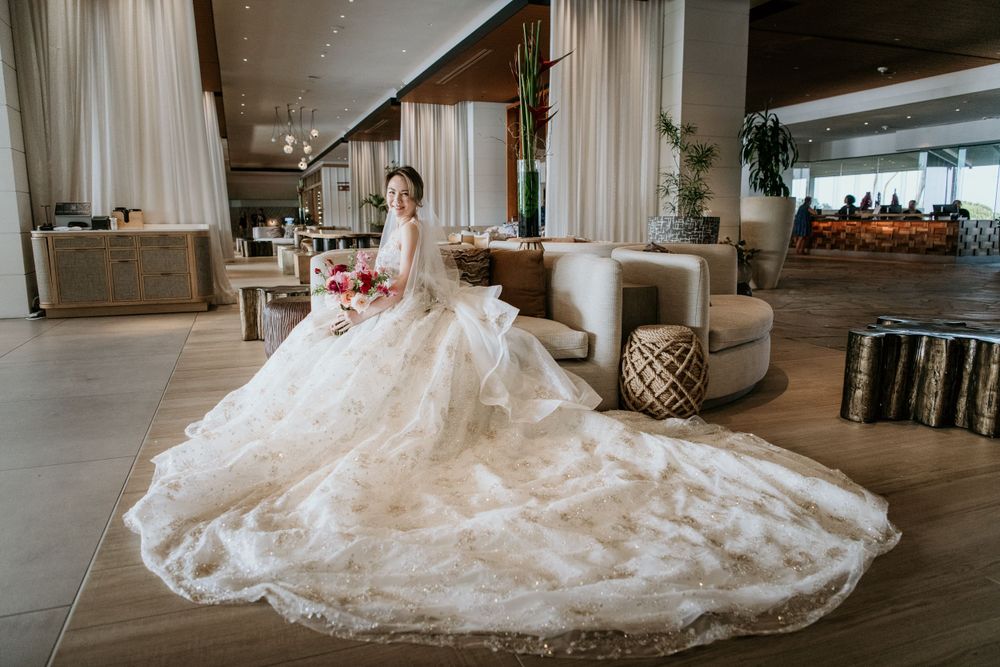 An elegant white lace wedding gown with a dramatic cathedral train spreads across a modern luxury hotel lobby.