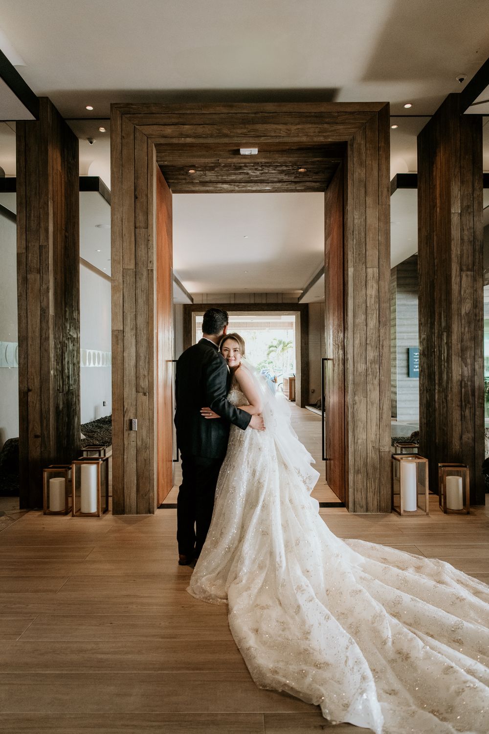 A beautiful wedding photo in a rustic wooden hallway with lanterns and a long flowing lace dress train.