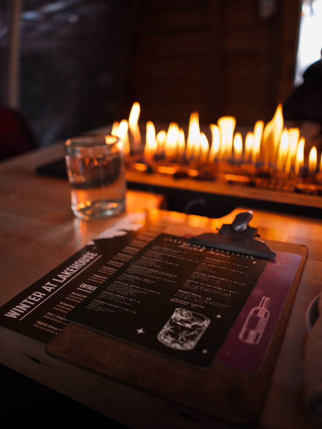 Menu cards displayed on a dark table illuminated by a row of glowing candles.