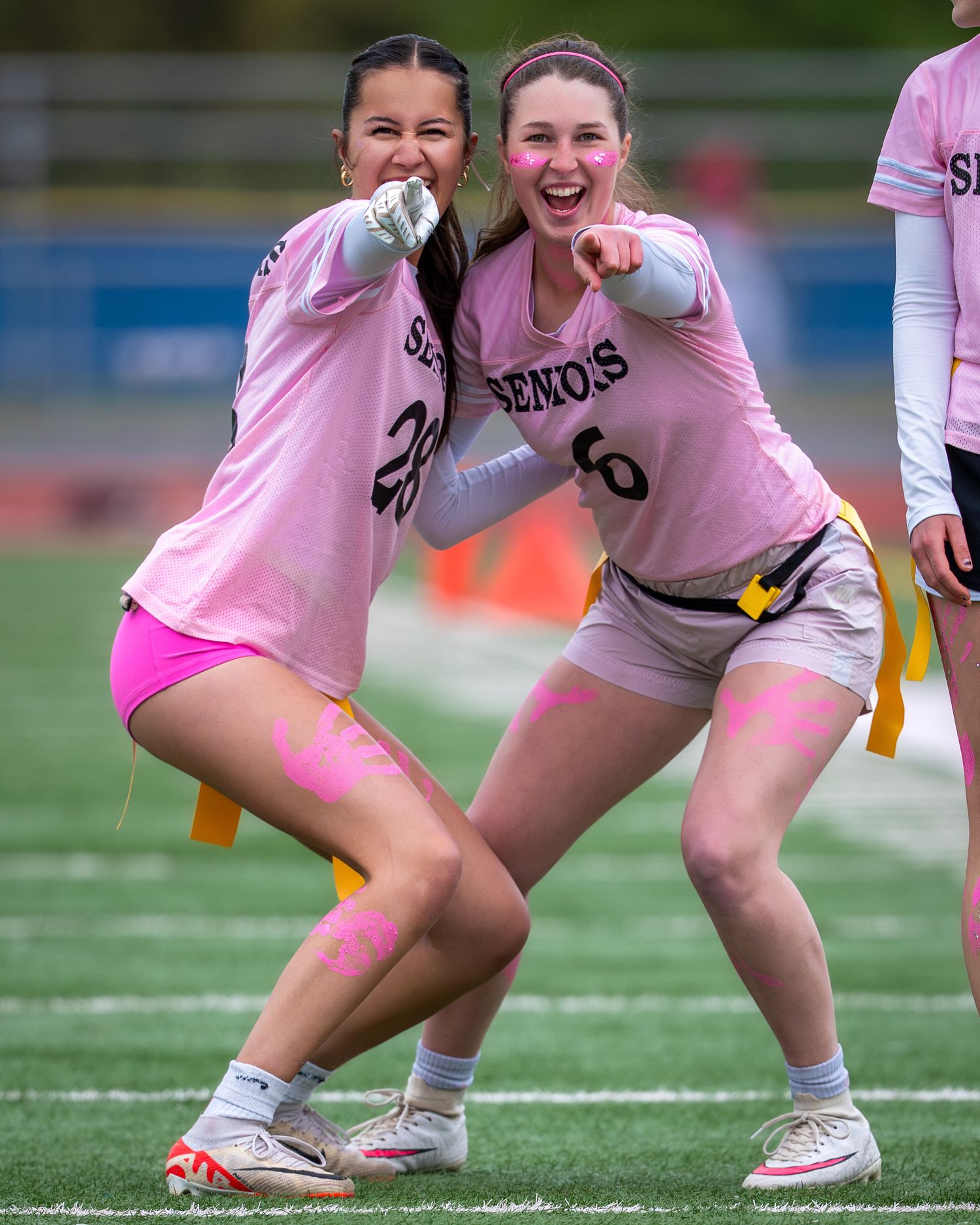 Two flag football players in pink jerseys celebrate together on a sports field during a game.