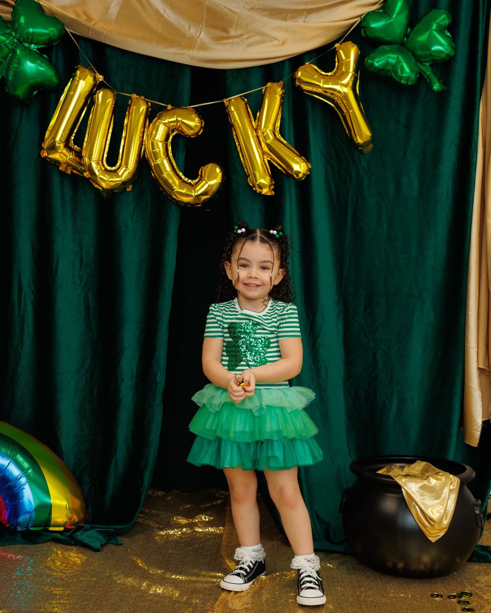 Green and gold St Patrick's Day party setup with balloon letters spelling LUCKY against emerald curtain backdrop.