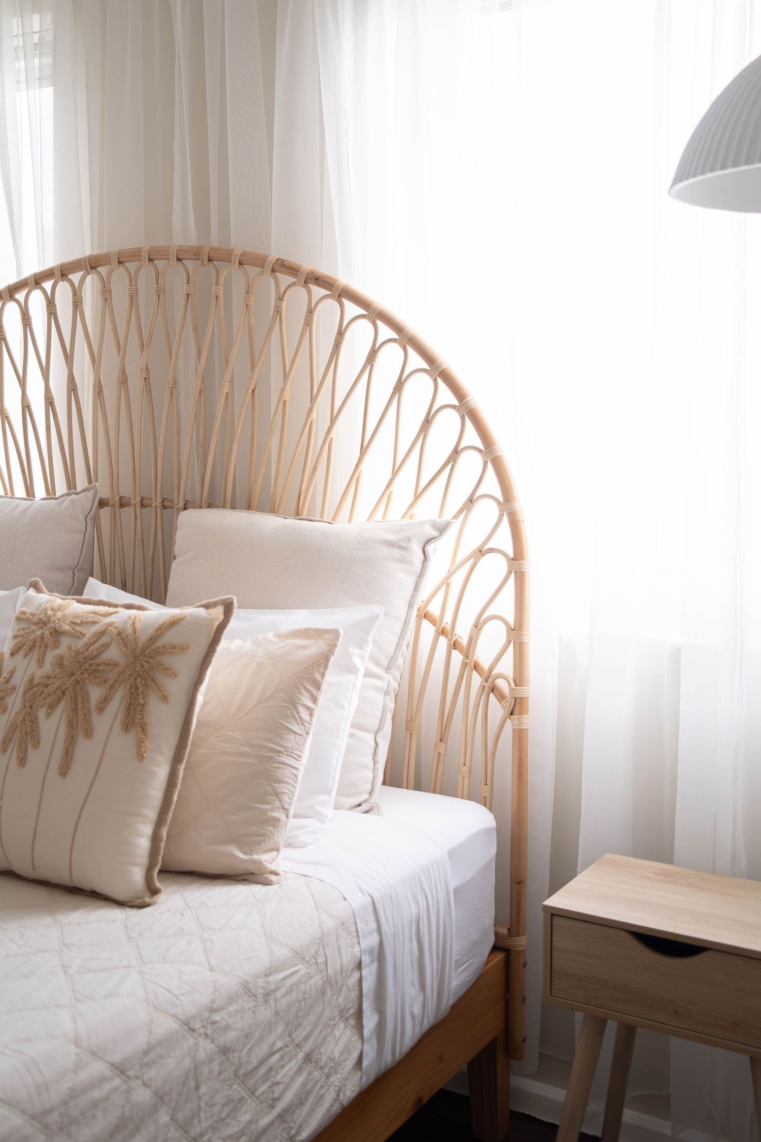 Natural rattan headboard bed with white bedding and beige throw pillows next to a wooden nightstand in neutral bedroom.