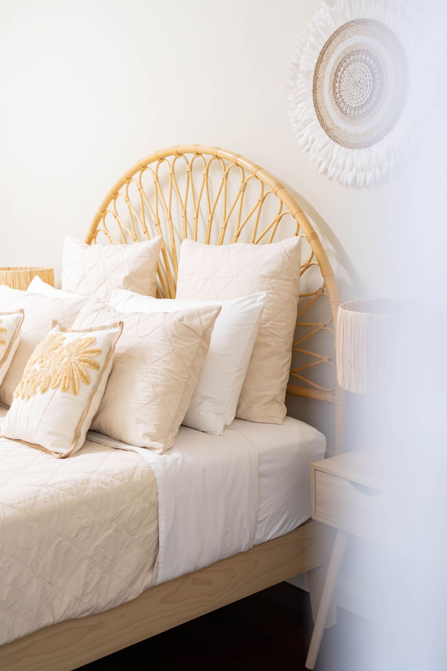 Cozy bedroom interior with rattan headboard, white bedding, decorative throw pillows and a sunburst ceiling medallion.