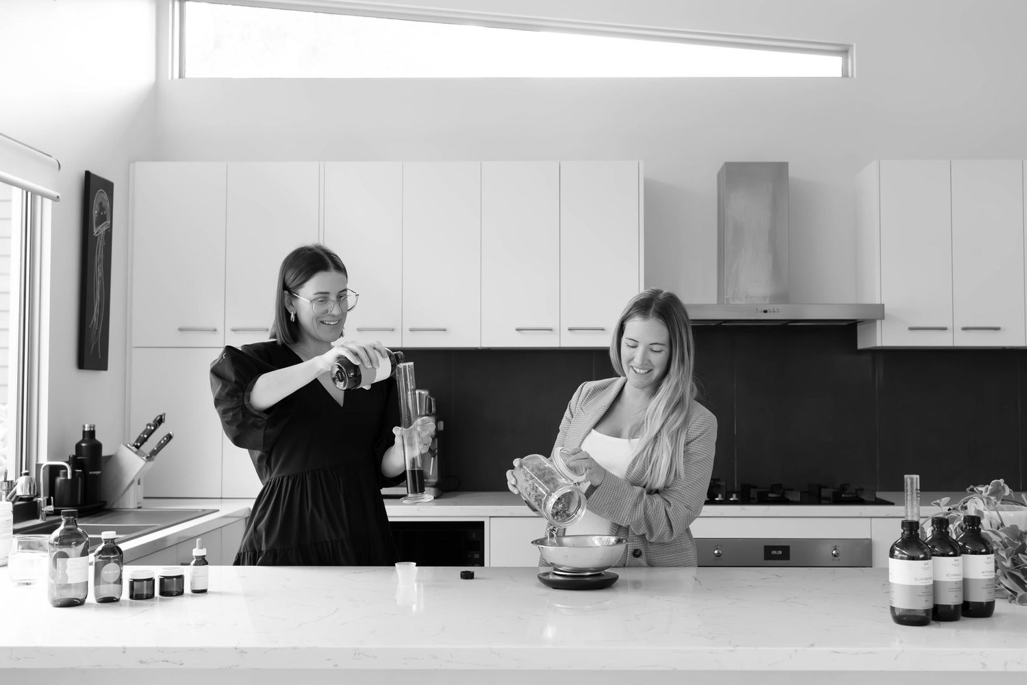 Two people preparing food together in a modern kitchen with white cabinets and black backsplash.