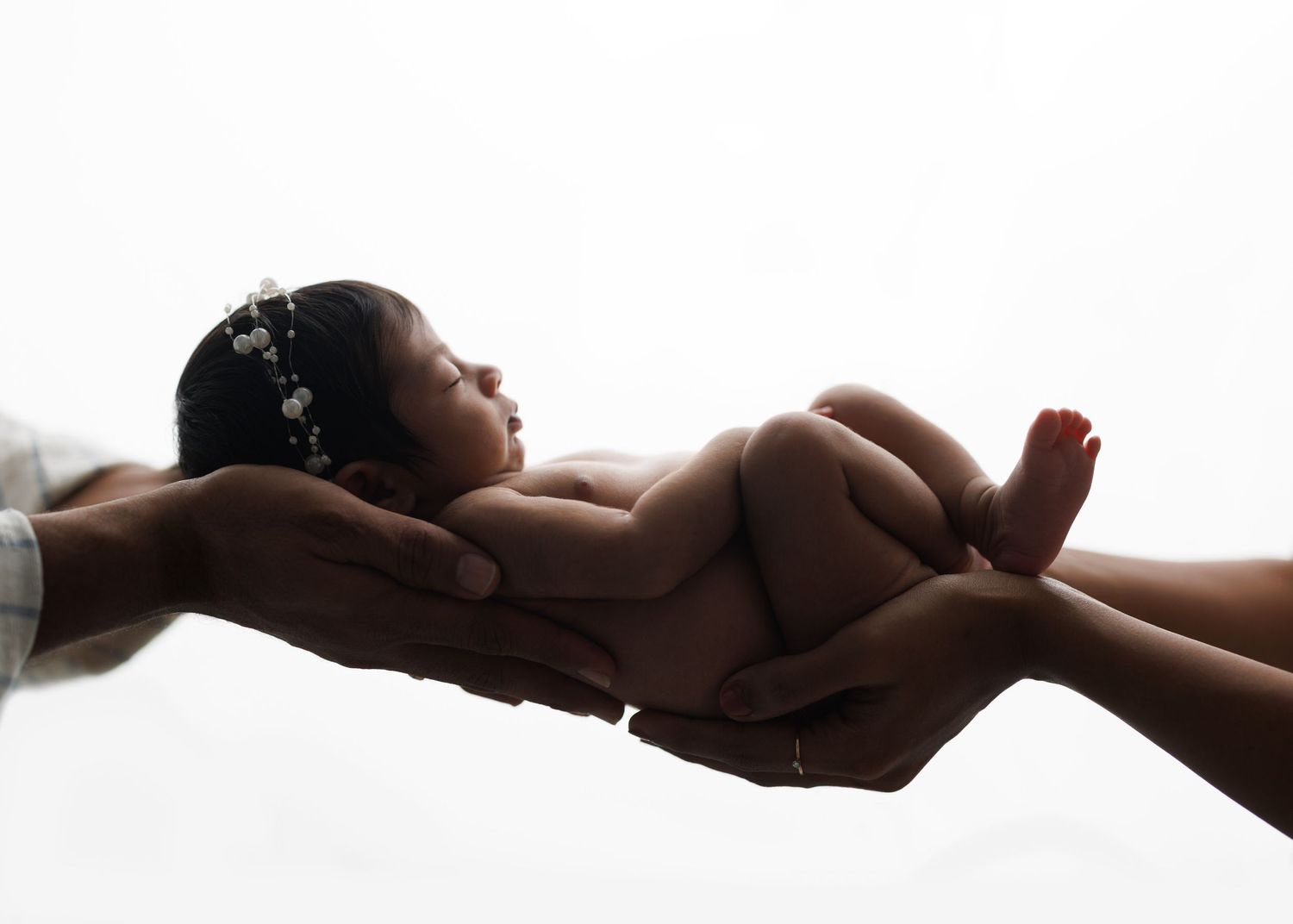 A newborn baby rests peacefully in gentle hands against a soft white background.